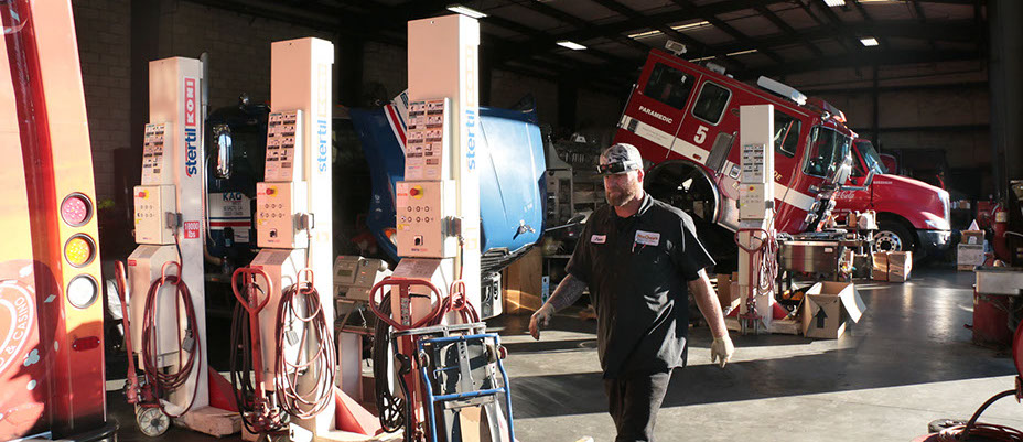 wide angle photo of the mccray mechanical shop, male worker walking by, nehind there is a blue truck and fire truck beign repaired.