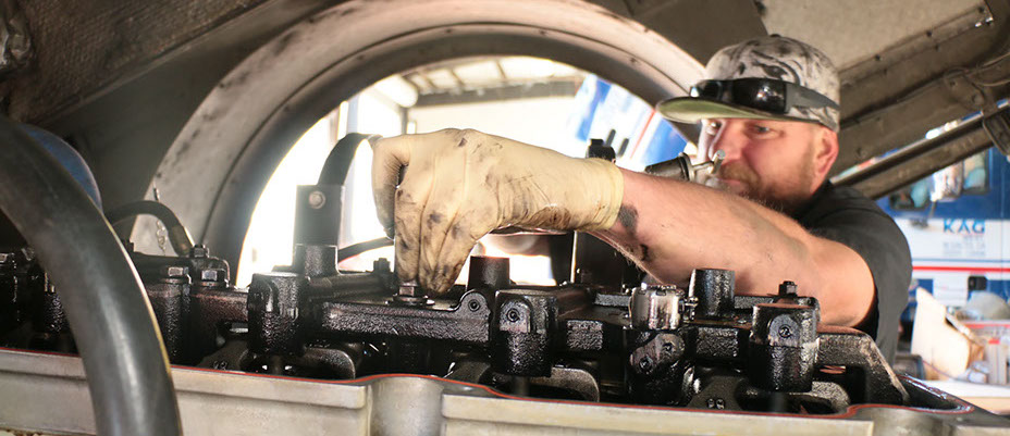 Mechanic working on truck with an open engine head 