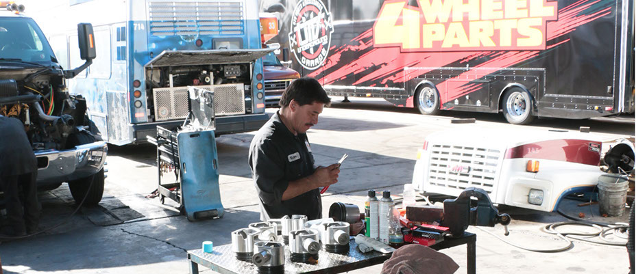 wide angle photo of mechanic inspecting parts with 3 trucks on background.