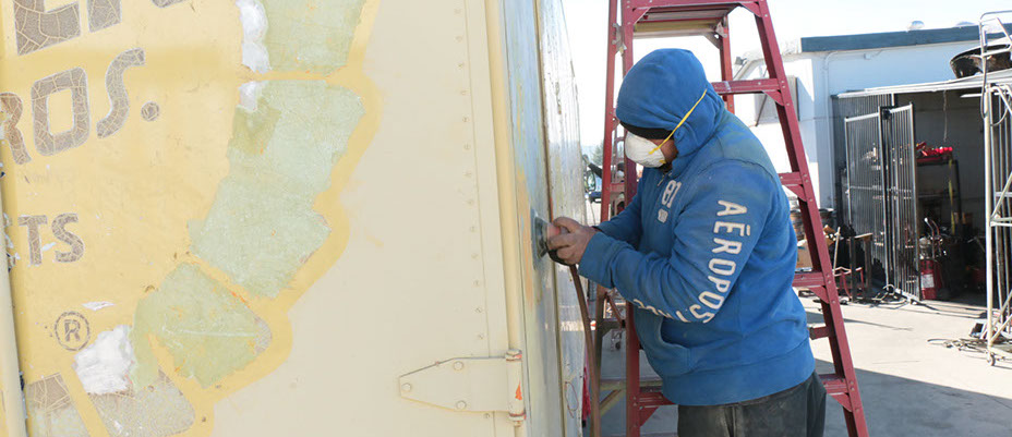 body shop worker wearing mask buffing the right side of a truck's cargo